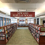 Thumbnail: Shelves full of books create a walkway straight forward with a sign above displaying New and Popular Books.