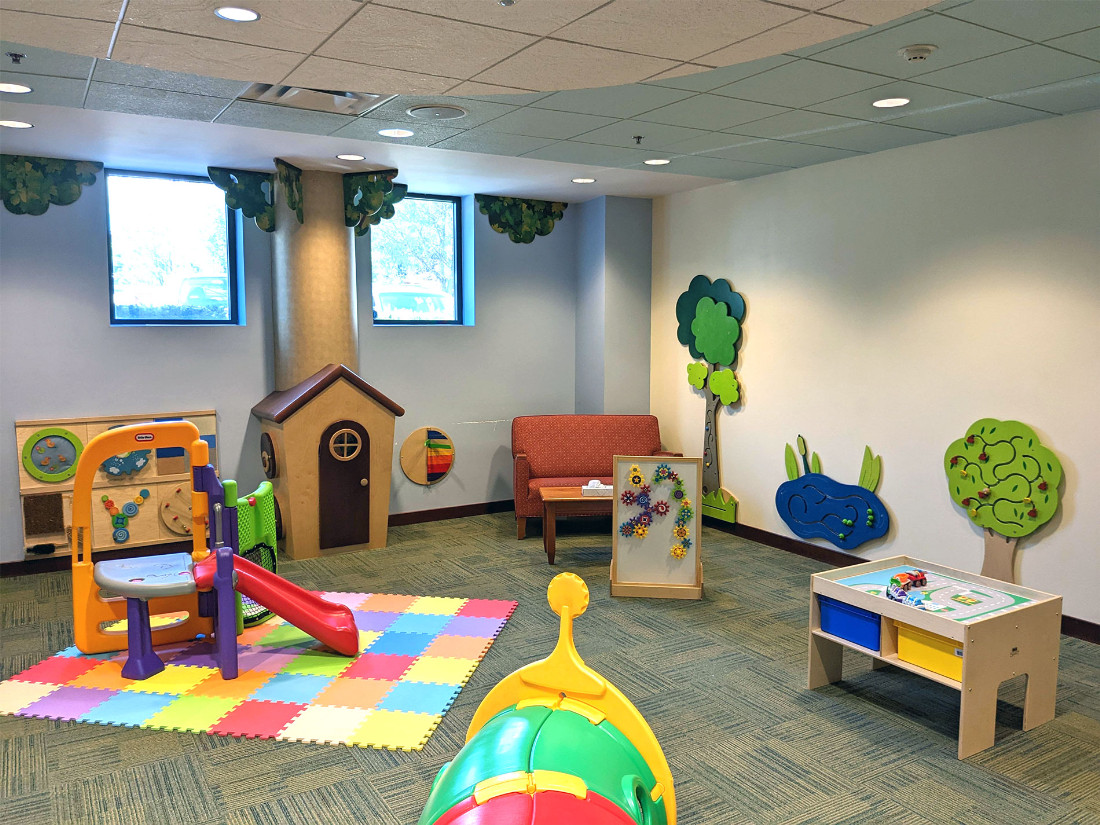 An indoor miniature “playground”, wall-mounted tactile play-and-learn toys, a tiny tree-themed house, and various other interactive items.