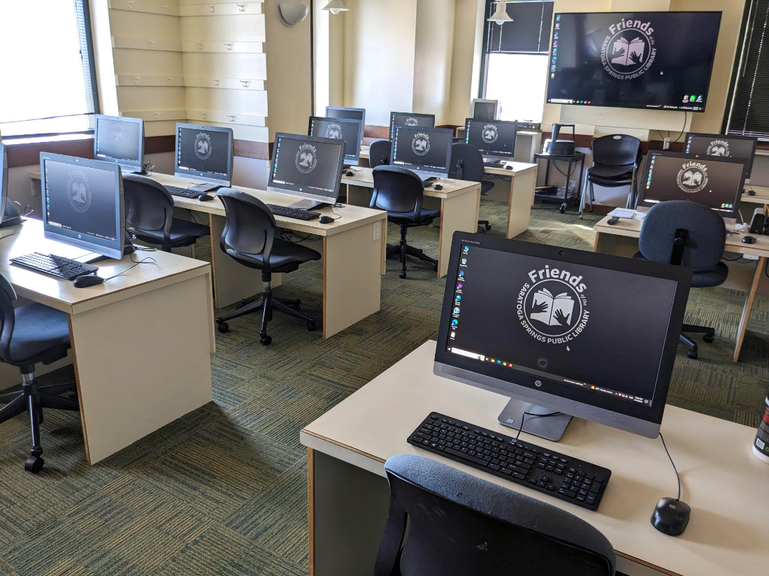 A perspective of the room, showing computers in rows, all turned on and loaded to the desktop.
