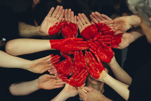 A jumble of arms reaching towards eachother, in the center a red heart is painted on many hands.