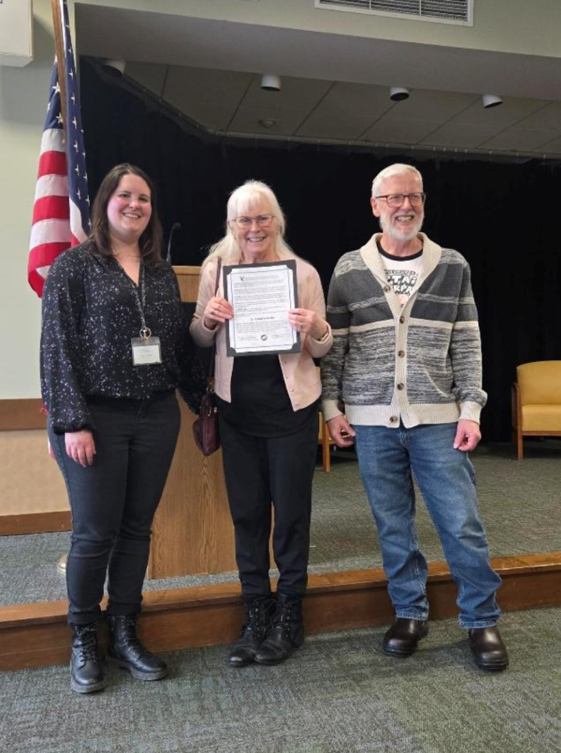 Two people stand beside the honoree holding a certificate of achievement.