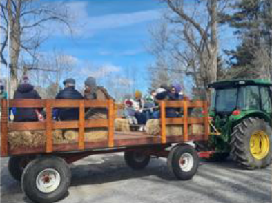 A tractor pulls a group of people along in a hayride-for-seats trailer.