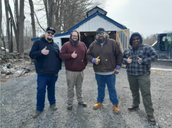 The workers of Maple Leaf Farms stand in front of the sugar shack, all smiling and giving a thumbs-up!