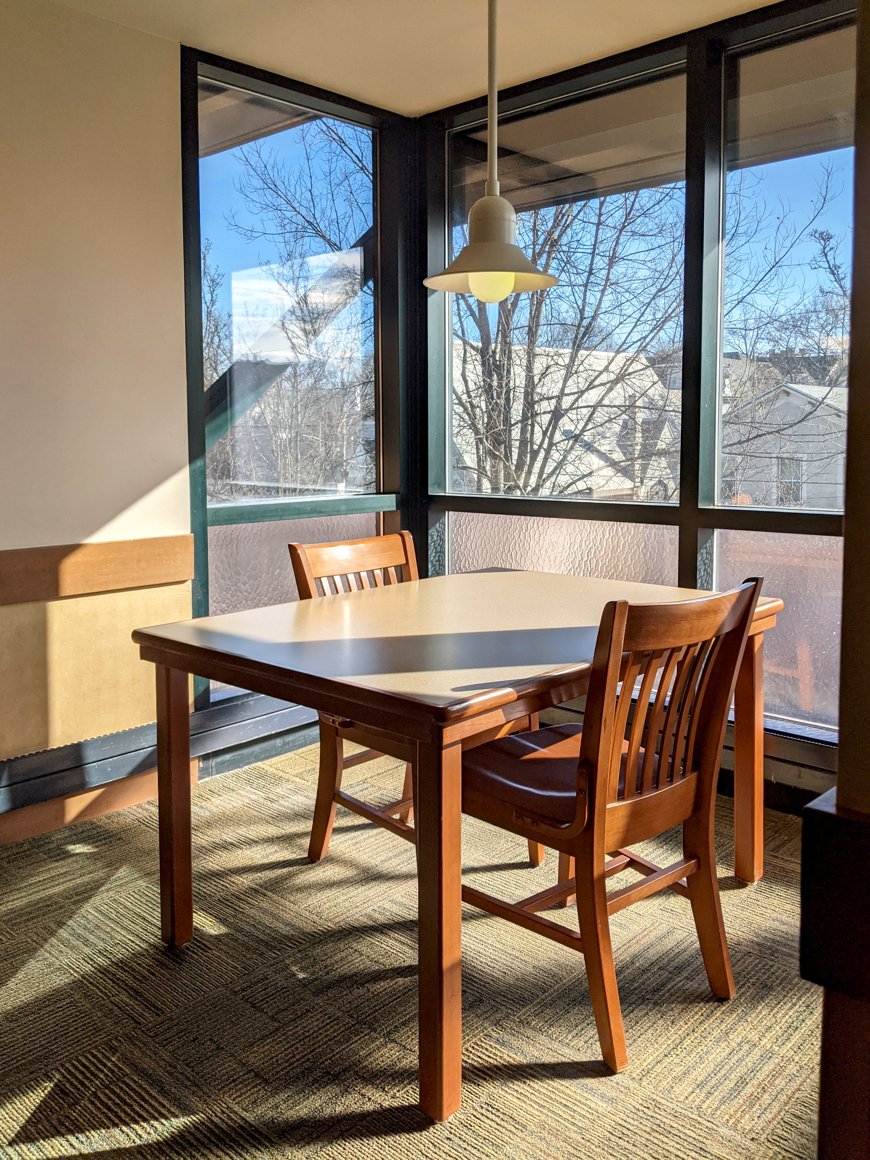 A table with two chairs in an alcove with a single pendant light, and sinlight shining through the three sides of the alcove onto the table.