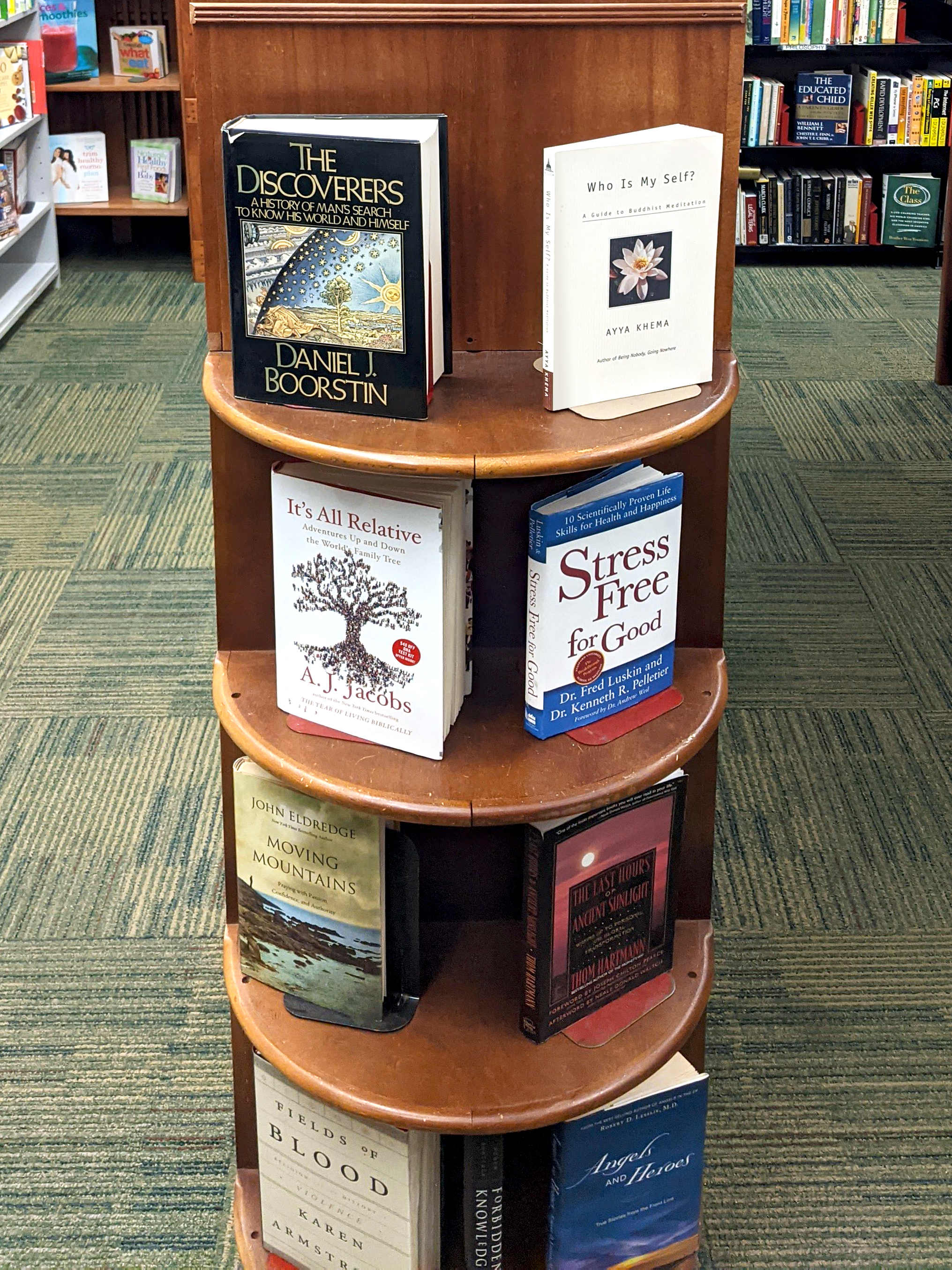 8 books displayed on a round, wooden shelf-end, vertically. There are 4 shelves with two books each.