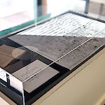 Thumbnail: Glass-topped display case protecting historic items as well as an historical map.