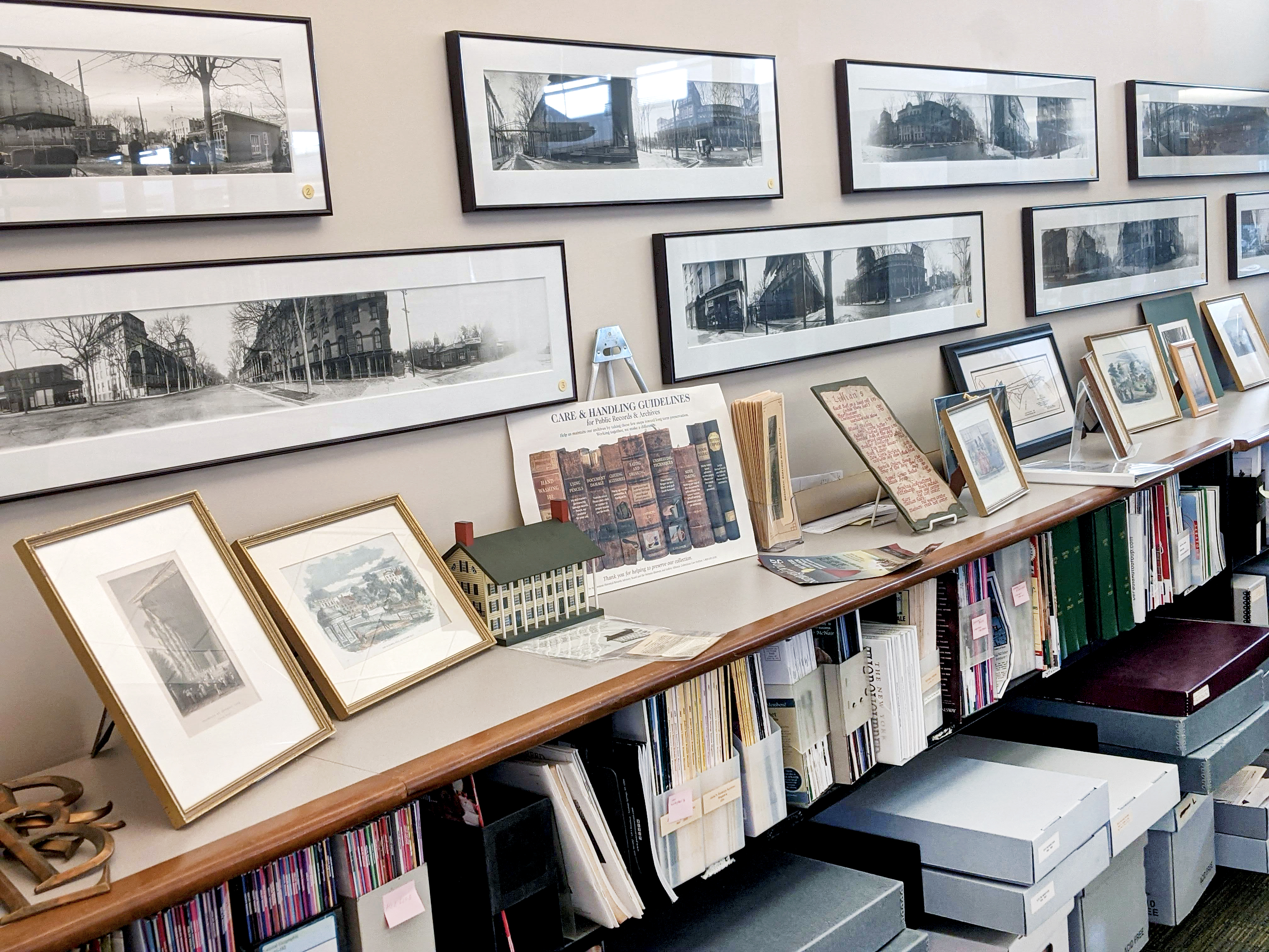 Material on a back shelf along a wall, with very early panoramic photographic prints of the Saratoga Springs area.