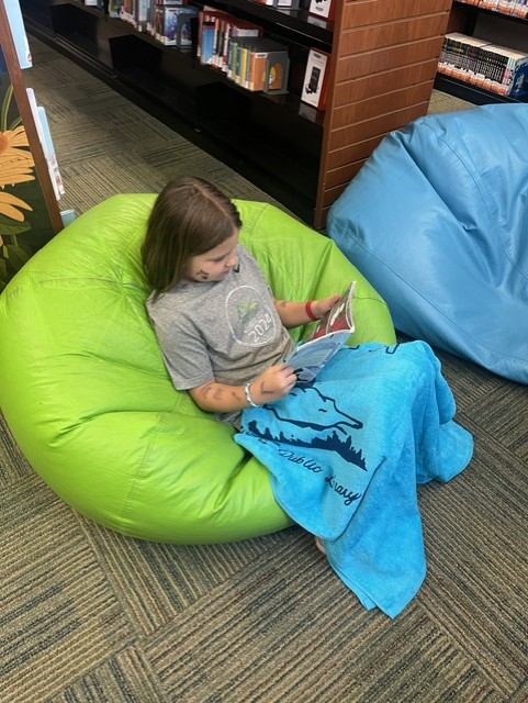 a child is reading in a bean bag wearing a turquoise summer reading towel
