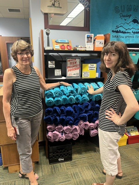 two library employees wearing matching shirts show off the library branded summer reading towels