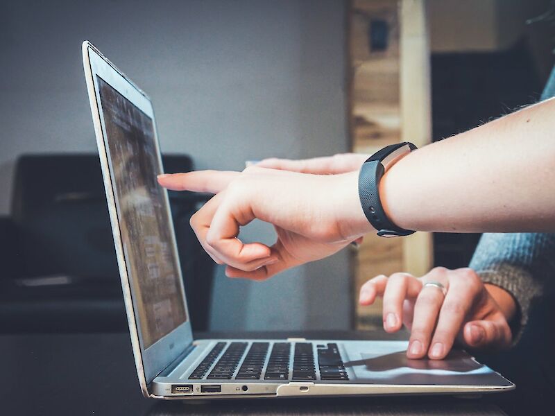 Close-up view of an opened laptop, two sets of hands reviewing what’s on the screen. Photo by John Schnobrich, Unsplash.