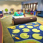 Thumbnail: A play place with a padded log bench, lily pad carpet, and scattered play things.