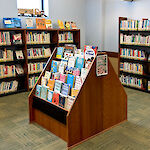 Thumbnail: A small floor standing stack of selected items in front of two large shelves against corner walls full of books.