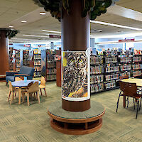 Tree-like columns, decorative wooden chairs, and shelves with animal-inspired endcap artwork withmany books on shelves.
