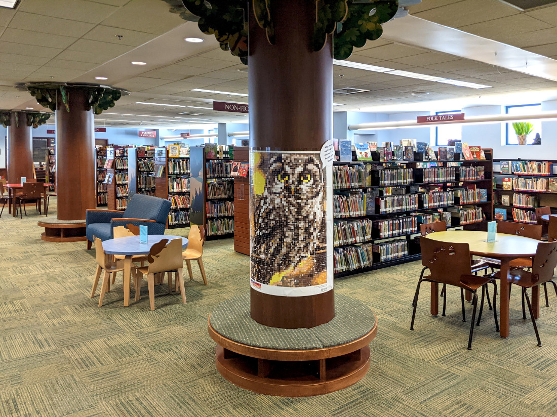 Tree-like columns, decorative wooden chairs, and shelves with animal-inspired endcap artwork withmany books on shelves.