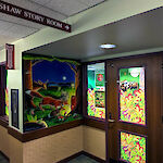 Thumbnail: Doorway entryway. Lit up room seen through windows. Painted wall mural, and a sign above the entryway which reads: CRAWSHAW STORY ROOM