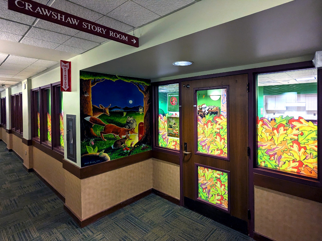 Doorway entryway. Lit up room seen through windows. Painted wall mural, and a sign above the entryway which reads: CRAWSHAW STORY ROOM
