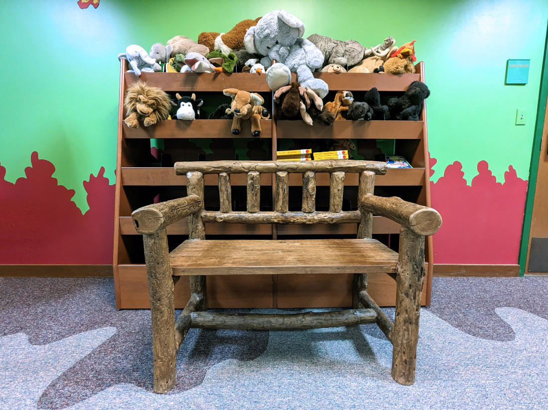 A large wooden timber chair sits in front of a wooden shelving unit, with stuffed animals loaded throughout.