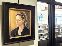 Images are hung on columns within a hallway. The nearest artwork is of a woman painted in period style, with a golden hue backdrop, brunette hair with golden highlights, and a black material around her shoulders.