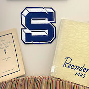 Saratoga Springs Senior High School’s Varsity Patch on the wall, between two examples of school yearbooks, titled “Recorder.”