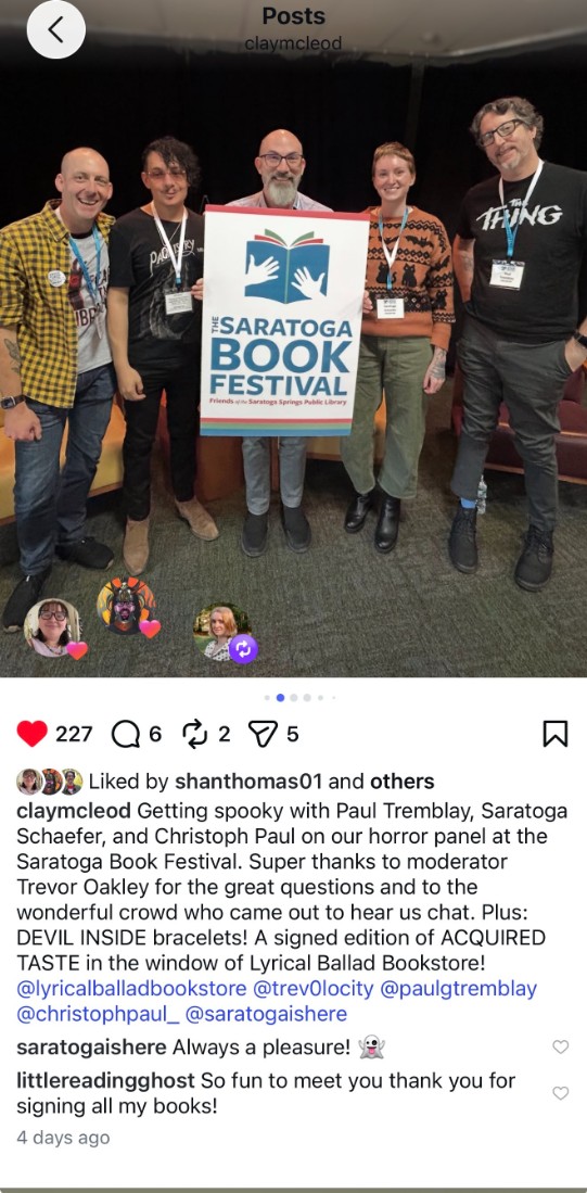 Five people stand together on a stage behind a Saratoga Book Festival sign, smiling for a group photograph. The festival’s logo is displayed prominently on the sign in front of the group.
