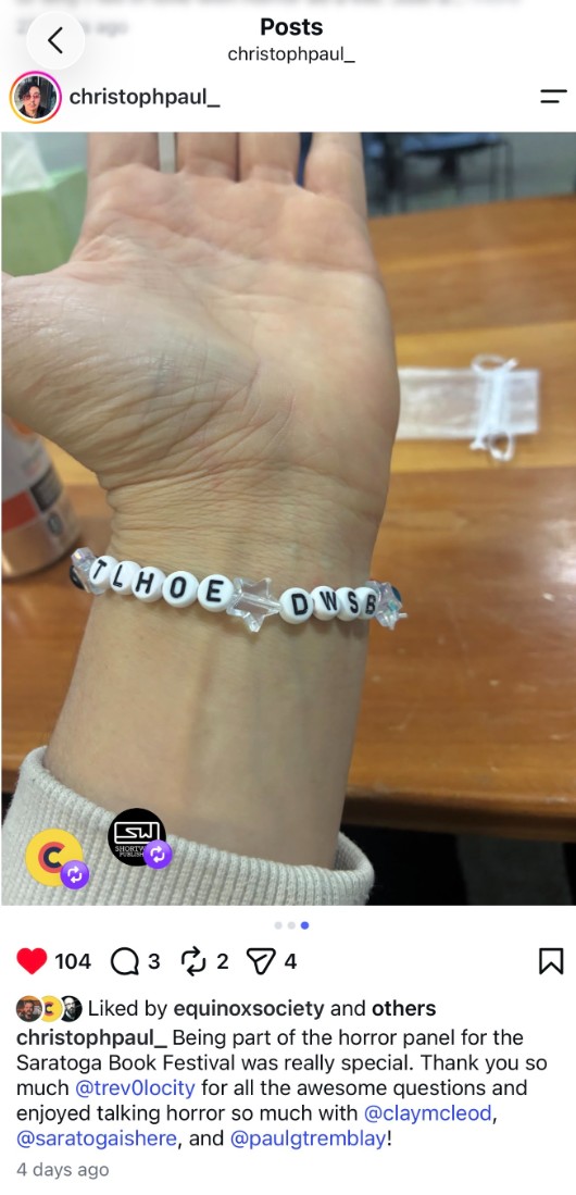 A close-up photograph of a wrist wearing a white beaded bracelet. The bracelet spells “TLOHE DWSB” with a clear star-shaped bead in the center. A wooden table is visible.