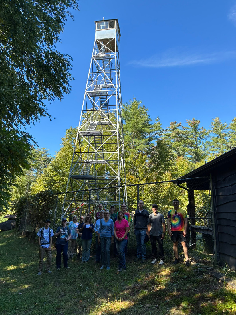 A group of adults are standing under a steel fire tower