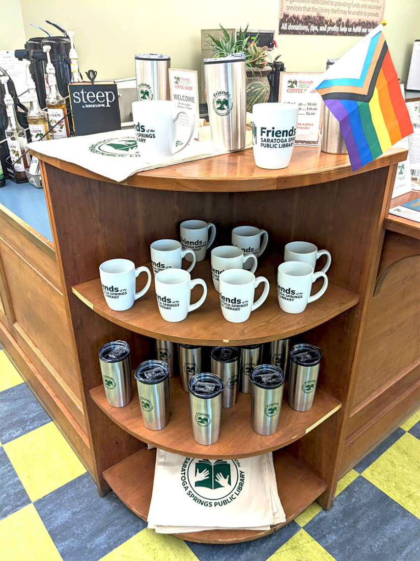 Decorated cloth shopping bags, ceramic and travel mugs fill an end-shelf’s display area for purchase.